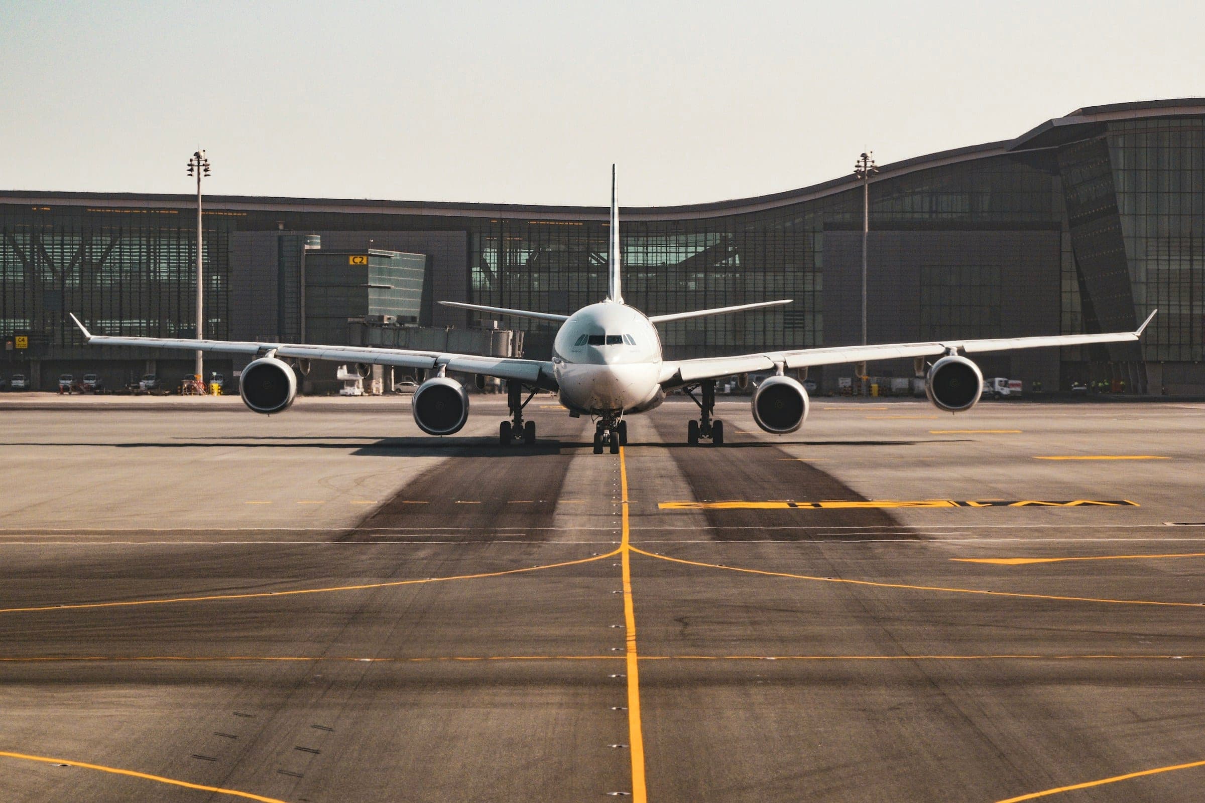 A four-engined widebody airliner taxiing head-on towards the camera in front of a long, low modern terminal.
