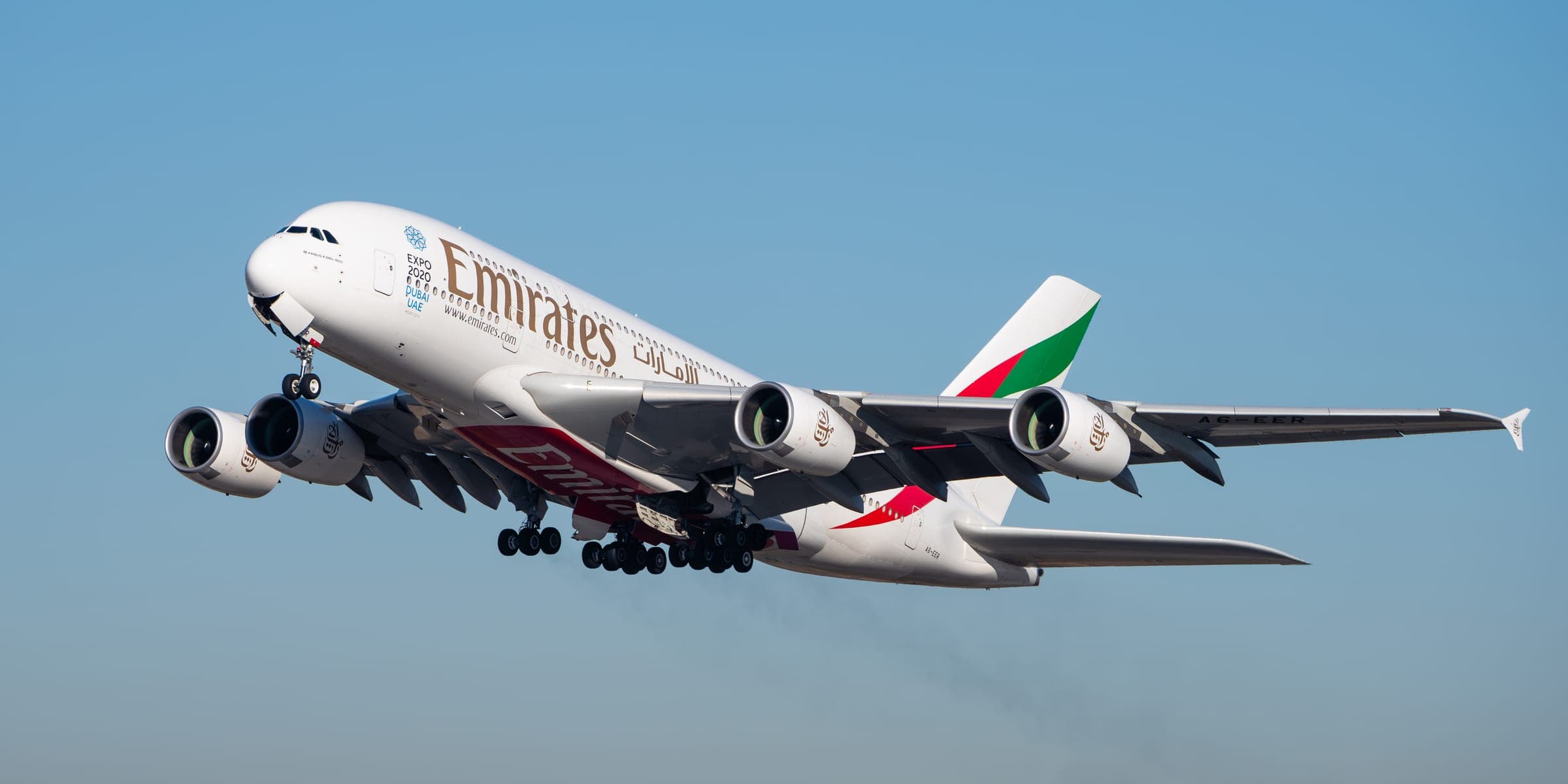 An Emirates Airbus A380 in a steep climb against a clear blue sky shortly after departure.