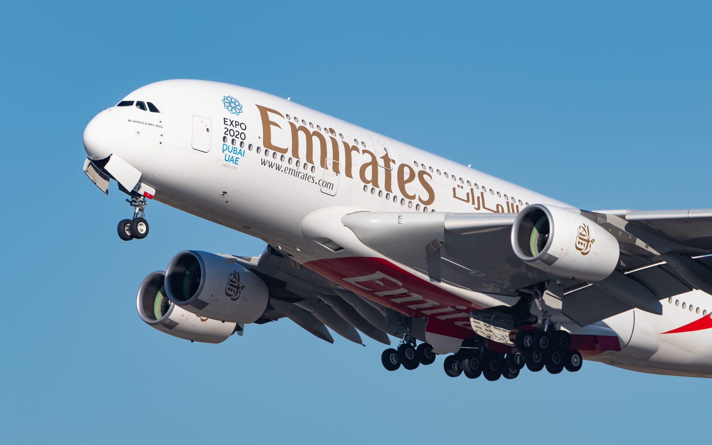 An Emirates Airbus A380 climbing away after take-off with its landing gear retracting, Expo 2020 Dubai decals on the forward fuselage.