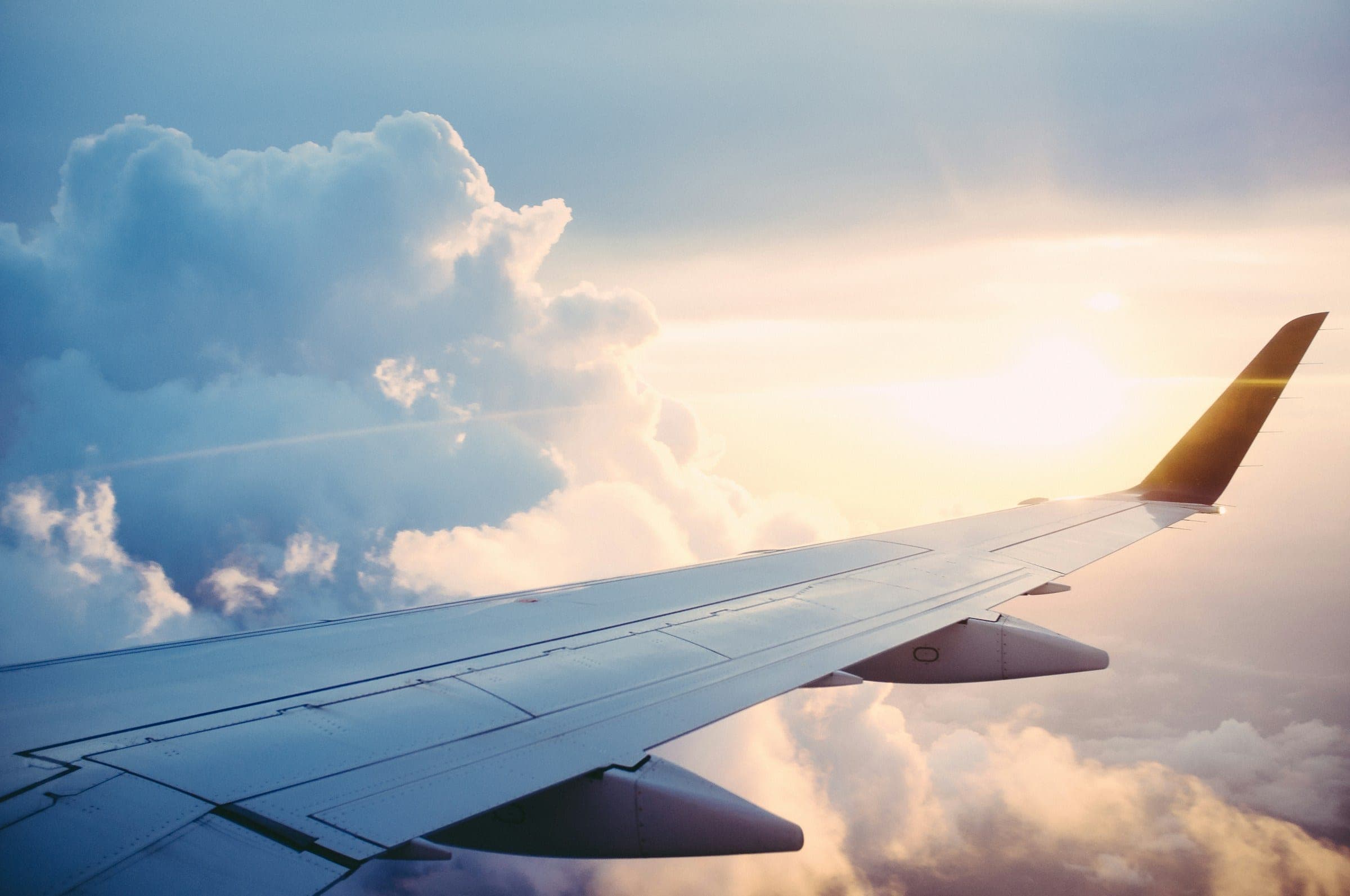 An airliner's wing above towering cumulus at sunset, the low sun flaring off the upturned winglet.