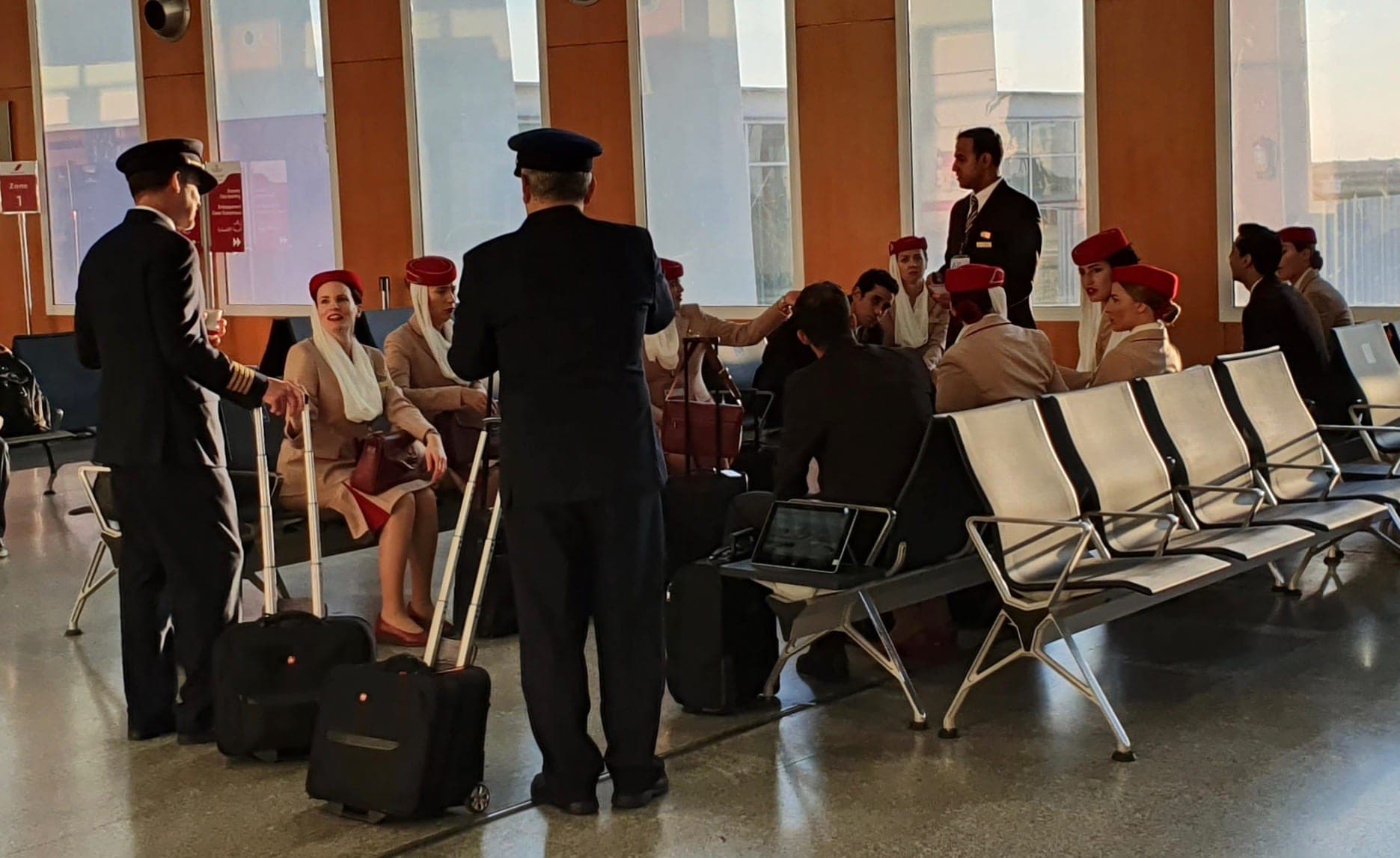 Emirates cabin crew and flight deck officers waiting with their cabin bags in an airport gate area between duties.