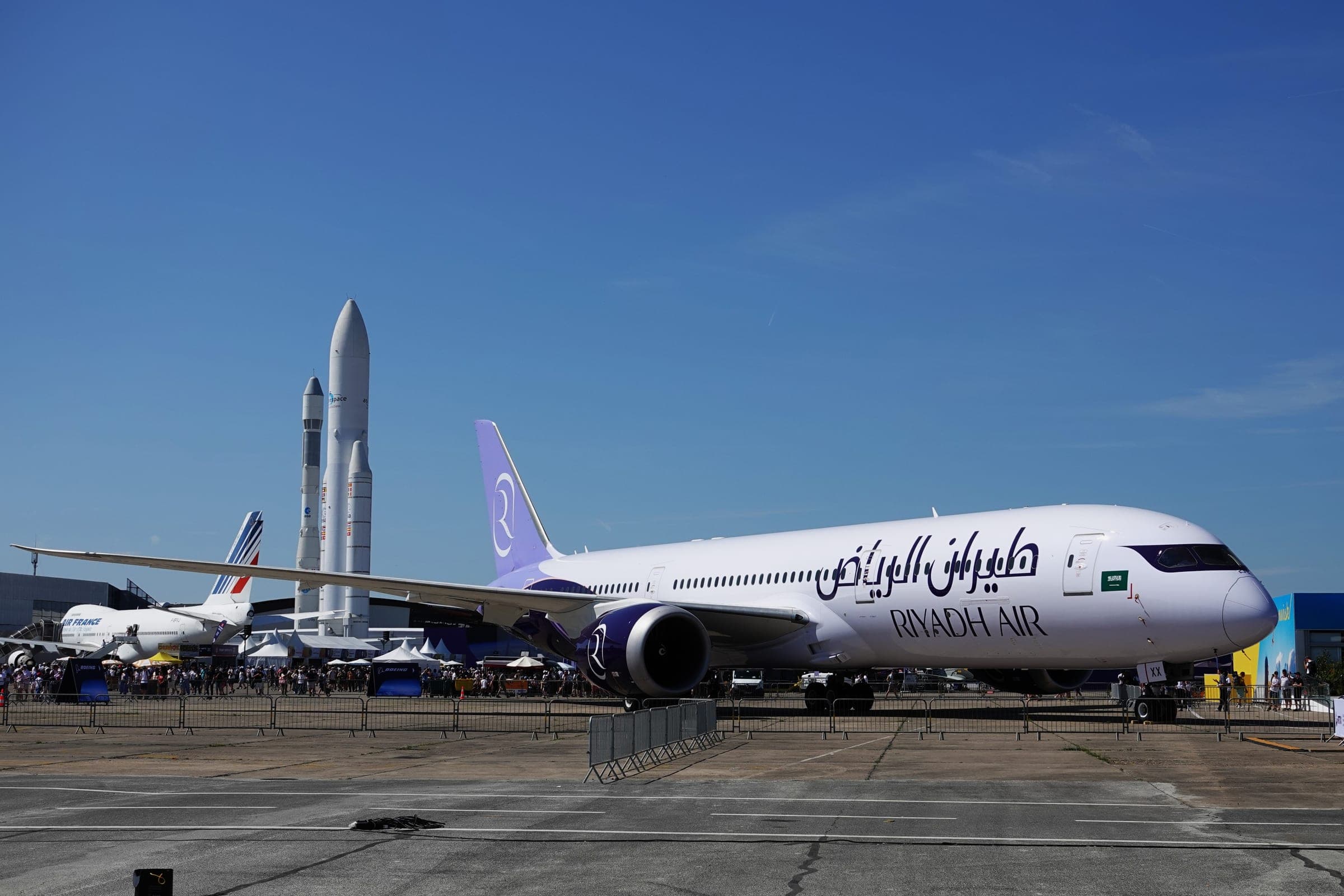 A Riyadh Air Boeing 787-9 Dreamliner, registration HZ-RXX, on static display at the 2025 Paris Air Show, in white with a lavender tail and Arabic and English titles along the fuselage.